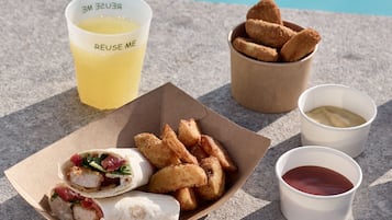 A meal consisting of a sandwich, fried items, and two drinks on a table by a pool.