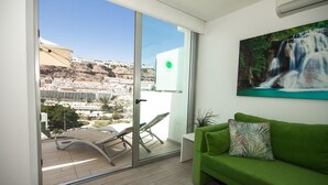 Un balcón con puerta de cristal, un sofá verde y un cuadro de una cascada.