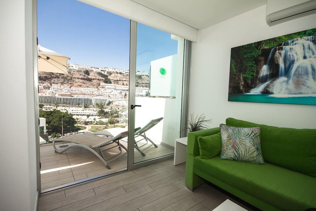 Un balcón con puerta de cristal, un sofá verde y un cuadro de una cascada.