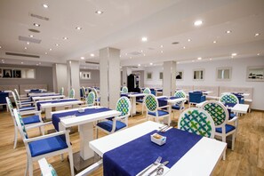 Un comedor con mesas y sillas blancas, manteles azules y un diseño moderno en el techo.