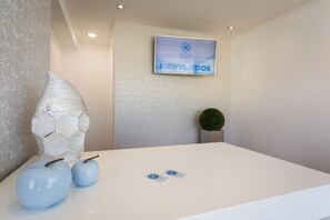 Un área de recepción con un cartel de bienvenida, una pared decorativa y una pequeña planta.
