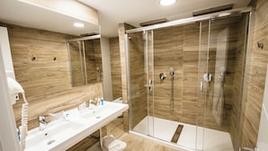 Un baño moderno con ducha envuelta en vidrio, lavabo blanco y paneles de madera.