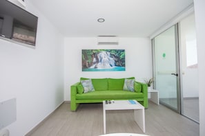 Uma sala de estar moderna com um sofá verde, uma mesa de centro e uma TV na parede.