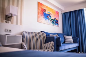 Quarto de hotel moderno com sofá azul, poltrona listrada e um quadro na parede.