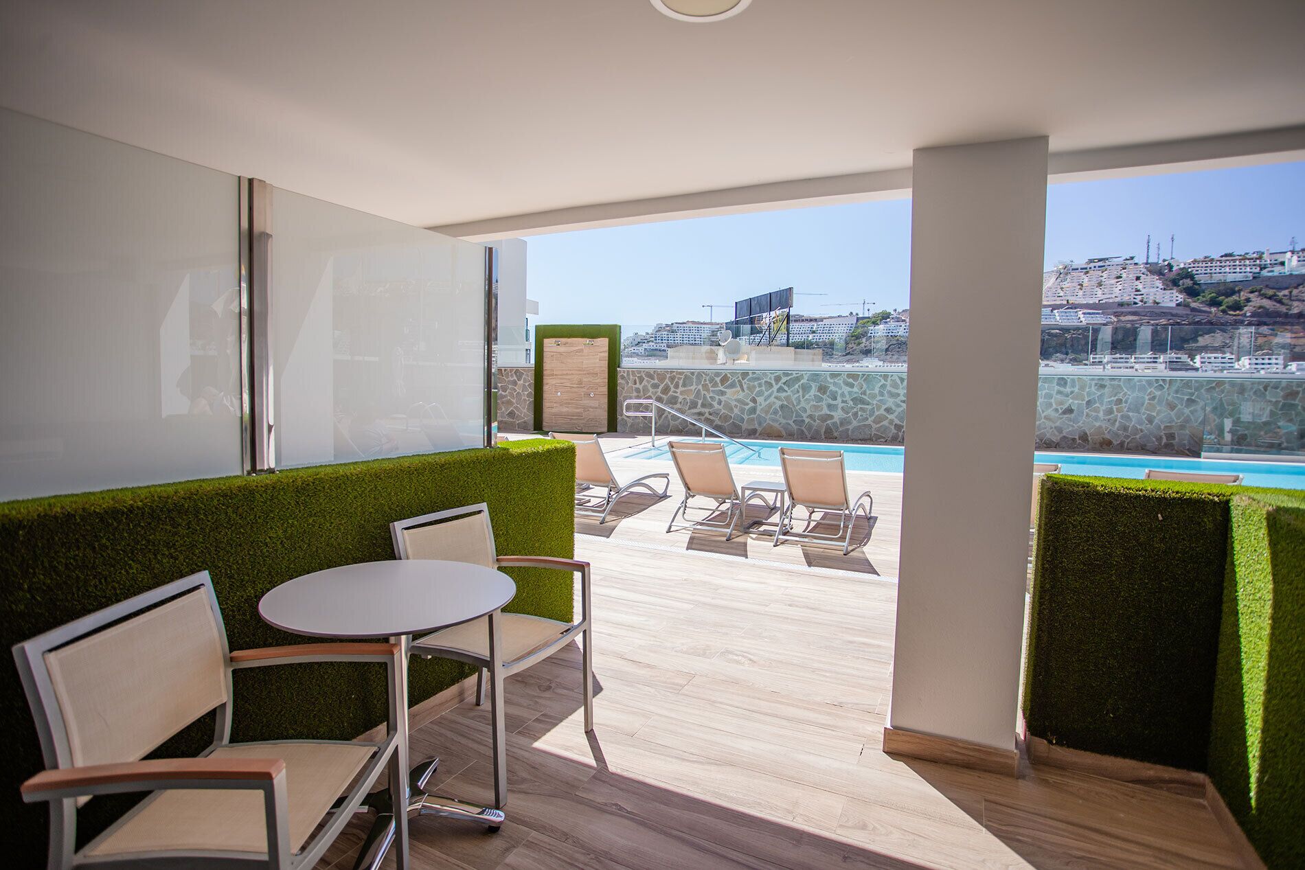 A balcony with a pool, lounge chairs, and a table.