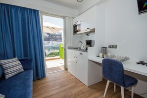 Ein kompakter Wohnraum mit Küchenzeile, einer Couch, einem Essbereich und Blick durch eine Glastür.