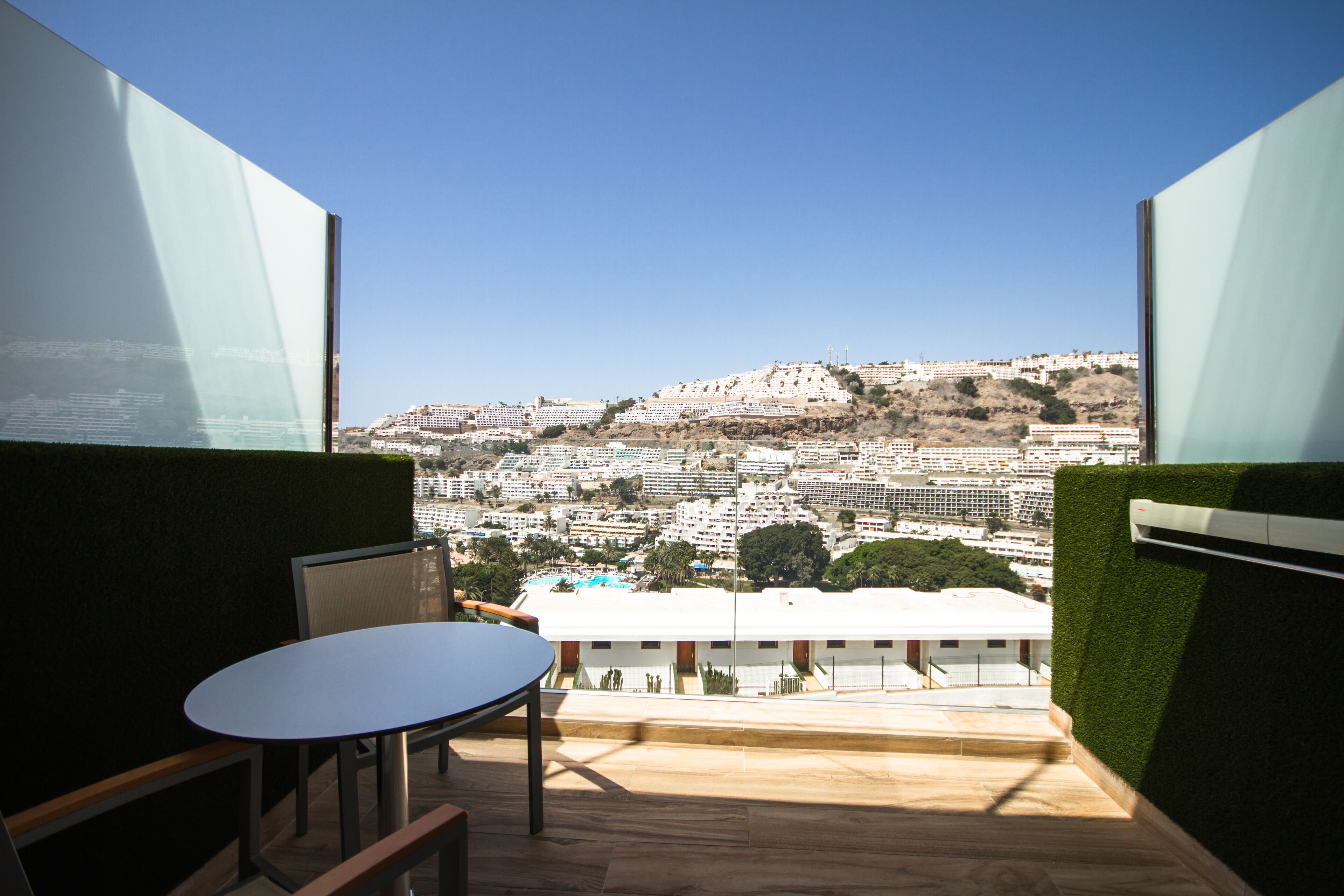 A balcony with a table and chairs, offering a view of a cityscape with buildings and greenery.