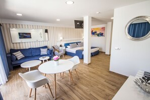 A modern hotel room with a sofa, two single beds, a dining area with a table and chairs, a TV mounted on the wall, and a painting on the wall. - IG Nachosol Atlantic & Yaizasol by Servatur (Mogan)