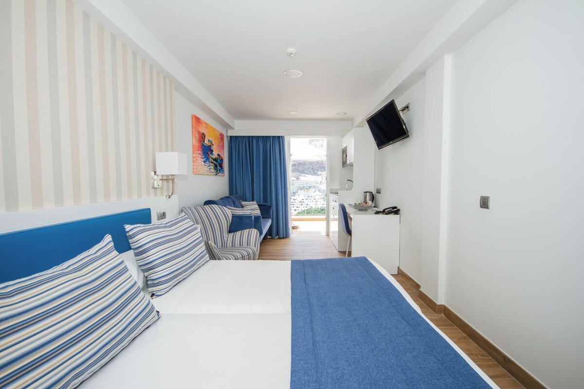 Habitación de hotel con cama, escritorio, televisión y vista a la ciudad.