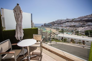 Un balcón con mesa y sillas, con vistas a un paisaje urbano costero que incluye edificios y una playa.