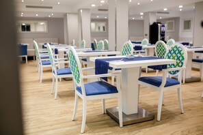 Un comedor con mesas y sillas blancas, cojines azules y piso de madera.