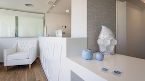 Un área de recepción con un mostrador blanco, una butaca blanca con diseño acolchado y un elemento decorativo en la pared.