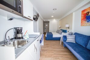Habitación de hotel compacta con kitchenette, una cama con cabecera azul y un cuadro en la pared.