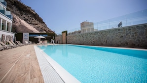 Una piscina con sillas de descanso y sombrillas, un muro de piedra y un edificio con un cartel que dice 'NACHSOL ATLANTIC HOTEL'.