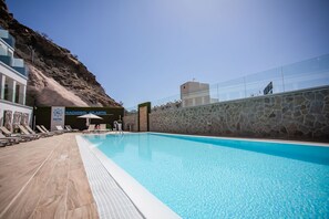 Una piscina con sillones de descanso y sombrillas, un muro de piedra y un edificio con un letrero que dice "NACHSOL ATLANTIC HOTEL".
