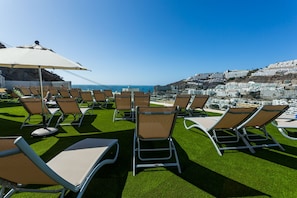 A rooftop terrace with rows of lounge chairs and a large umbrella, overlooking a coastal cityscape. - IG Nachosol Atlantic & Yaizasol by Servatur (Mogan)