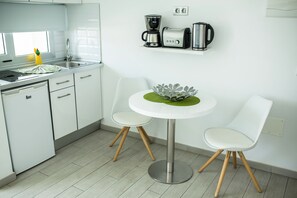 Eine moderne Küche mit weißen Schränken, einer Edelstahlspüle, einer Kaffeemaschine, einem Toaster und einem kleinen runden Tisch mit zwei Stühlen.