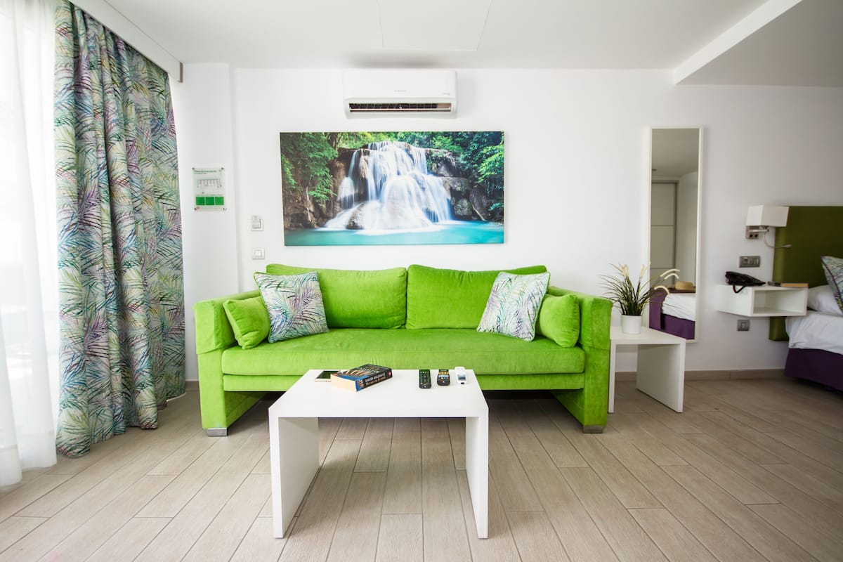 Una sala de estar moderna con un sofá verde, una mesa de centro blanca y un cuadro con motivo de cascada en la pared.