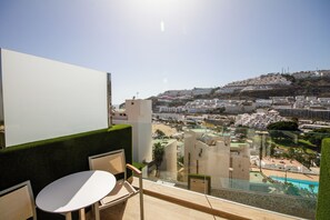 Un balcón con vista a un paisaje urbano costero, que incluye una playa y edificios en una colina.