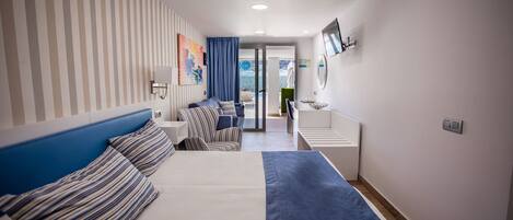 Ein Hotelzimmer mit Bett, einer Sitzecke mit Sofa und Sesseln, einem kleinen Tisch und einem Badezimmer mit Spiegel und Waschbecken.
