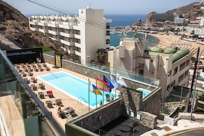 Un hotel con piscina, varias banderas y vista a la playa y al océano.