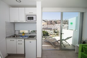 A compact kitchen with a microwave, sink, and cabinets, leading to a balcony with a view of a cityscape. - IG Nachosol Atlantic & Yaizasol by Servatur (Mogan)
