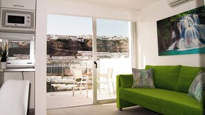 Una sala de estar moderna con un sofá verde, un cuadro de una cascada y vistas de la ciudad a través de un gran ventanal corredero.
