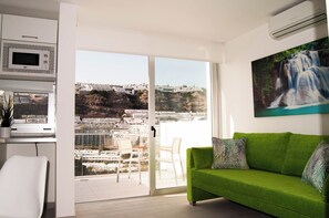 Una sala de estar moderna con un sofá verde, un cuadro de una cascada y vistas de la ciudad a través de un gran ventanal corredero.