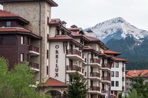 A multi-story hotel with balconies and a view of a snow-capped mountain. - Orbilux (Bansko)
