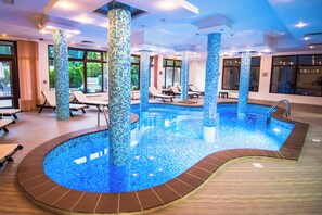 An indoor swimming pool with tiled walls and columns, surrounded by lounge chairs and a sunbed. - Orbilux (Bansko)