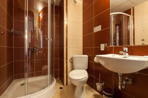 A bathroom with a glass-enclosed shower, a toilet, and a sink with a mirror above it.