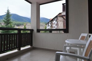 A balcony with a view of mountains and buildings, a white table, and a chair. - Orbilux (Bansko)