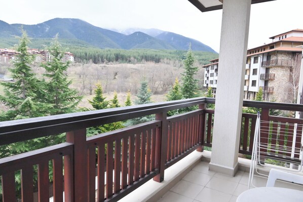 A balcony with a view of mountains, trees, and a building in the background.