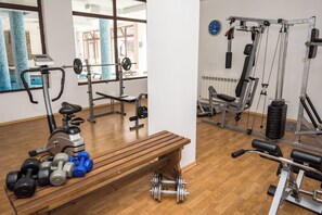Ein Fitnessraum mit Trainingsgeräten, einer Holzbank und Kurzhanteln.