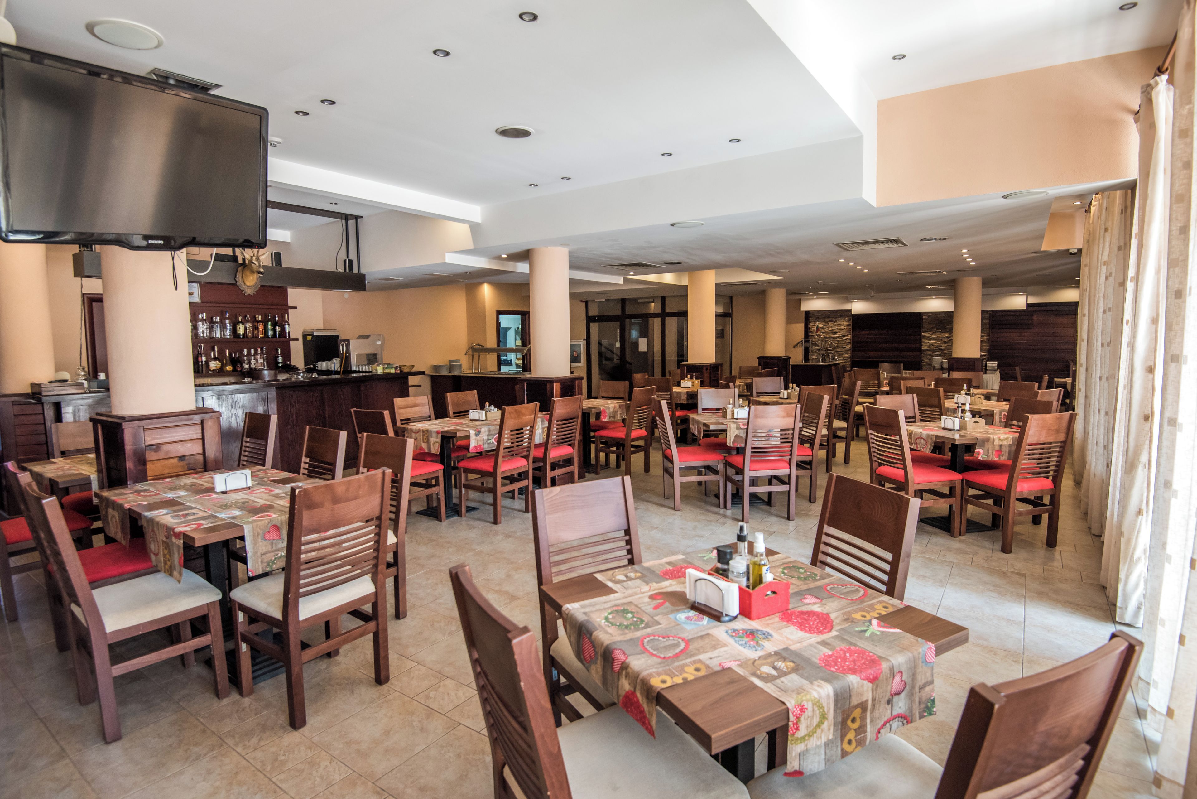 A restaurant with multiple tables and chairs, a bar area, and a television mounted on the wall.