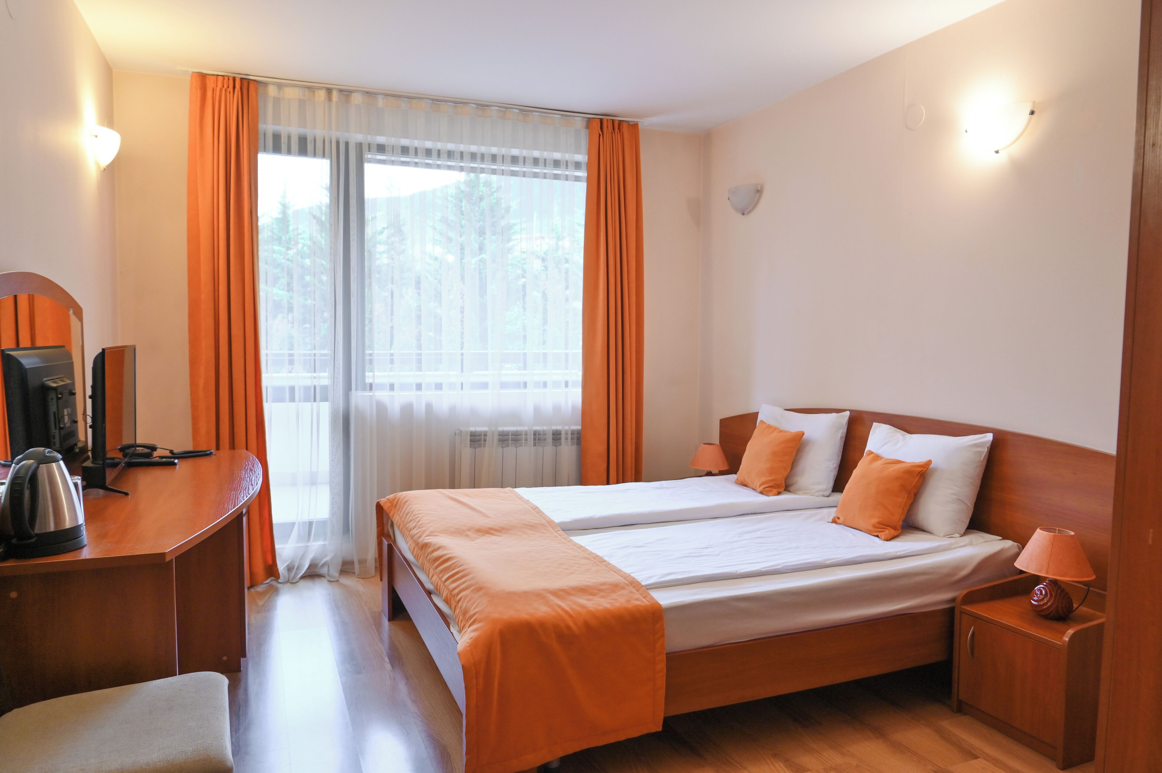 Hotellihuone, jossa on parivuode, työpöytä, jossa on vedenkeitin, tuoli ja yöpöytä, jossa on lamppu.