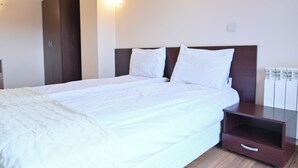 A neatly made bed with white bedding, a wooden headboard, and a small wooden nightstand with a drawer.