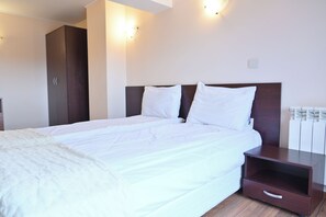 A neatly made bed with white bedding, a wooden headboard, and a small wooden nightstand with a drawer.