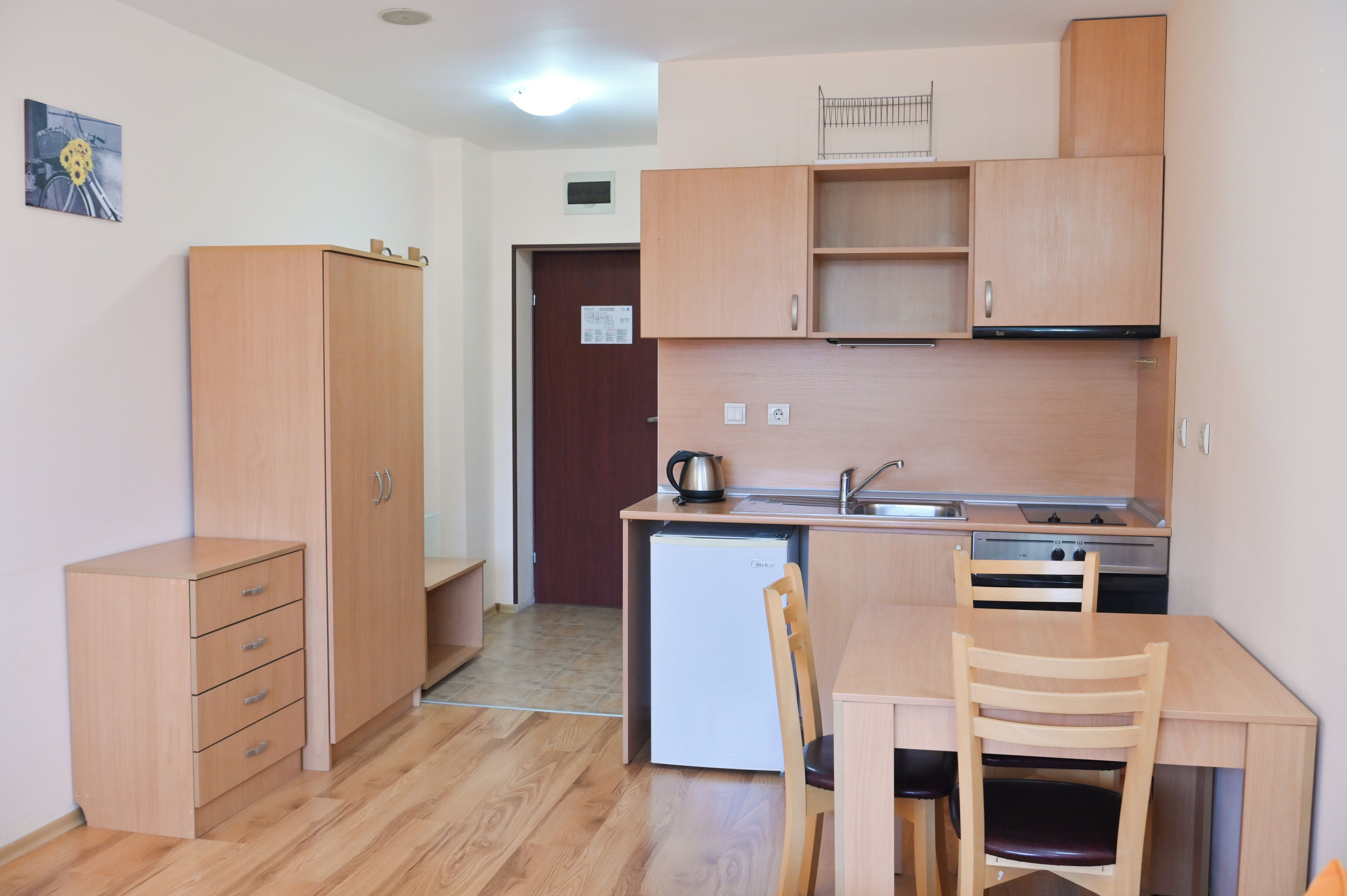 Une cuisine de taille réduite, dotée de meubles de rangement en bois, d’un réfrigérateur, d’un évier et d’une table à manger avec des chaises.