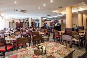 A restaurant with multiple tables and chairs, a bar area, and a mounted animal head decoration. - Orbilux (Bansko)