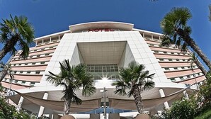 Un hôtel moderne à la façade incurvée, doté de plusieurs étages et bordé de palmiers au premier plan.