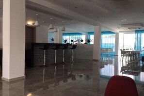 A modern hotel lobby with a reception desk, bar stools, and a dining area with tables and chairs. - Sunny Blue Hotel (Ayia Napa)