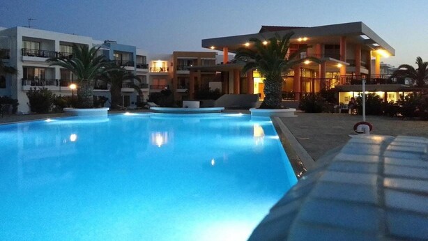A swimming pool with adjacent modern buildings, palm trees, and a clear sky.