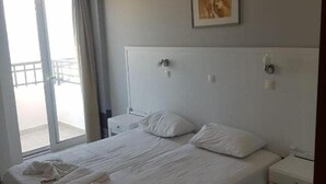 A hotel room with a large bed, a bedside table, a chair, and a view of the outside balcony.