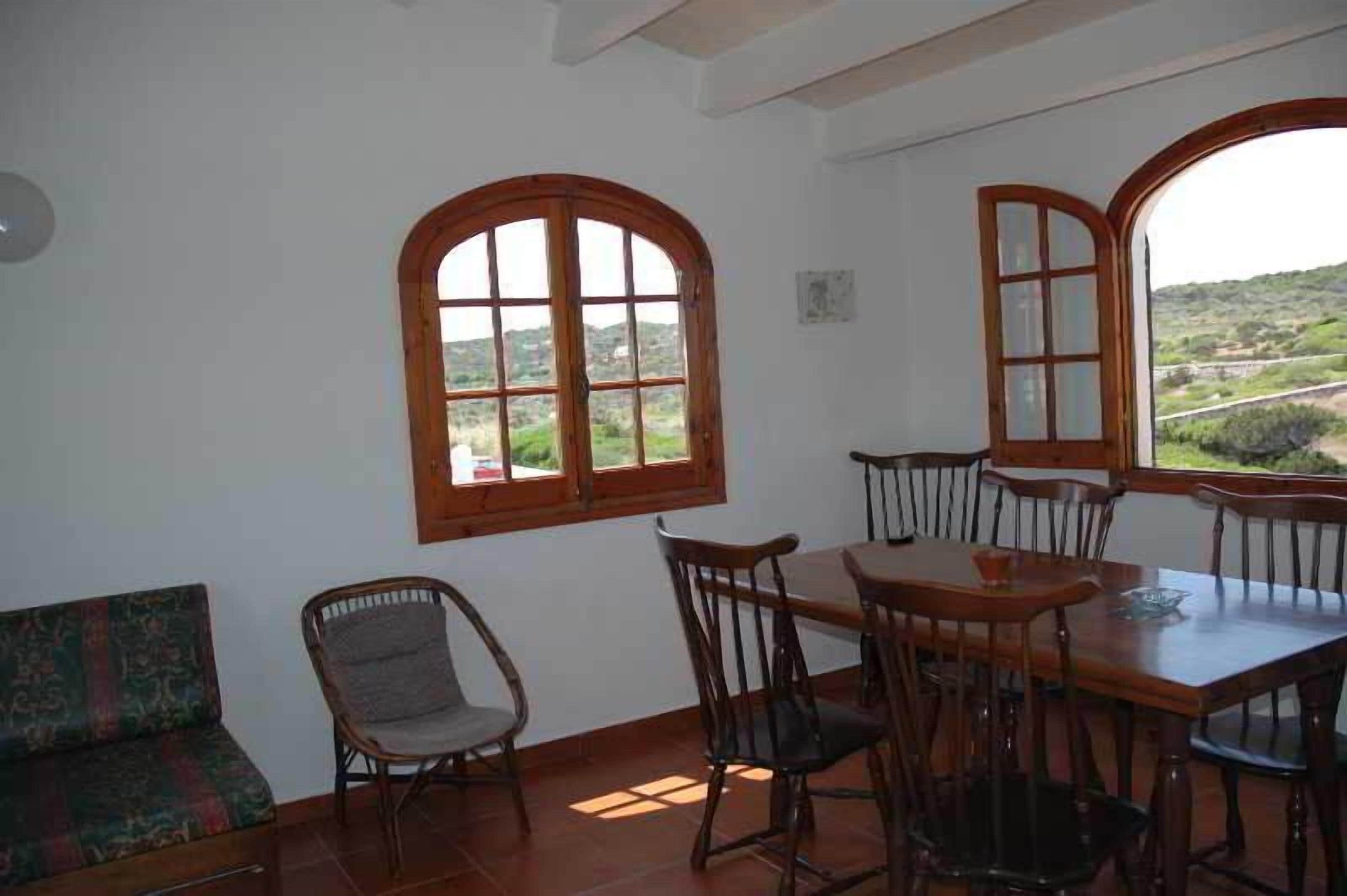 A dining area with a table and chairs, large arched windows with a view of greenery, and a patterned sofa.