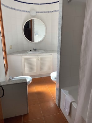 A bathroom with a round mirror, two sinks, a toilet, and a shower area.
