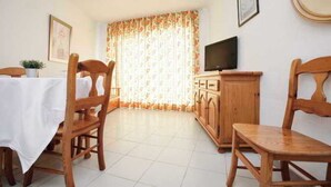 A room with a dining table, two wooden chairs, a television, and a cabinet.