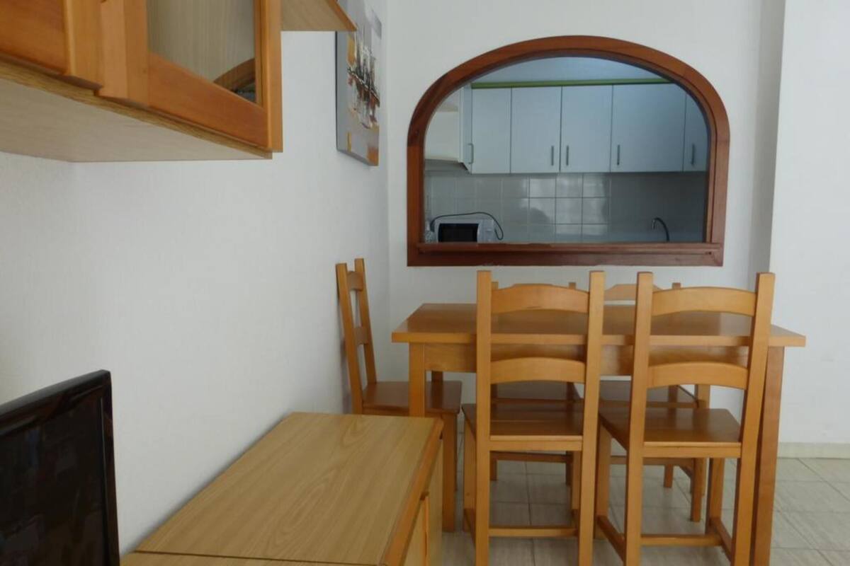 A compact kitchen with white cabinets, a wooden dining table with four chairs, and a small window above the sink.