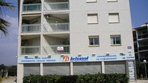 A multi-story building with balconies, a sign for 'brisasol' and 'Administración de Comunidades', and a closed garage door.