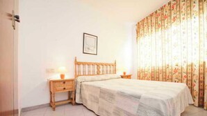 A bedroom with a wooden bed, two bedside tables, a framed picture on the wall, and floral curtains.